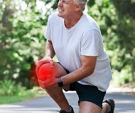 Man met grijs haar geknield op een pad, met zijn hand op zijn knie