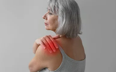 Vrouw in grijze top die haar hand naar haar schouder brengt